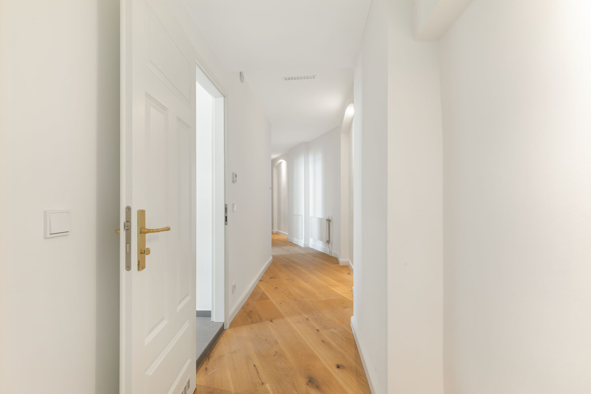 Heller Flur mit Holzboden und weißen Wänden in einem Wohnhaus.