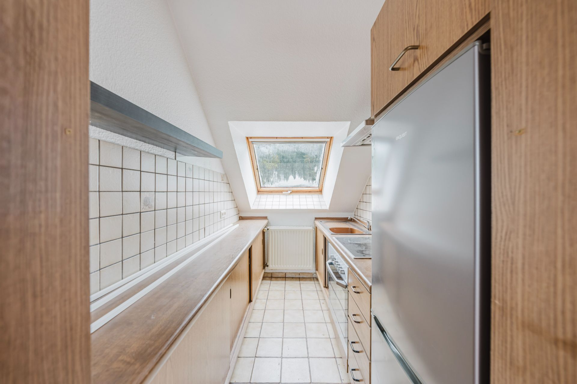 Schmale Küche mit Holzmöbeln, Fliesenboden und Dachfenster.
