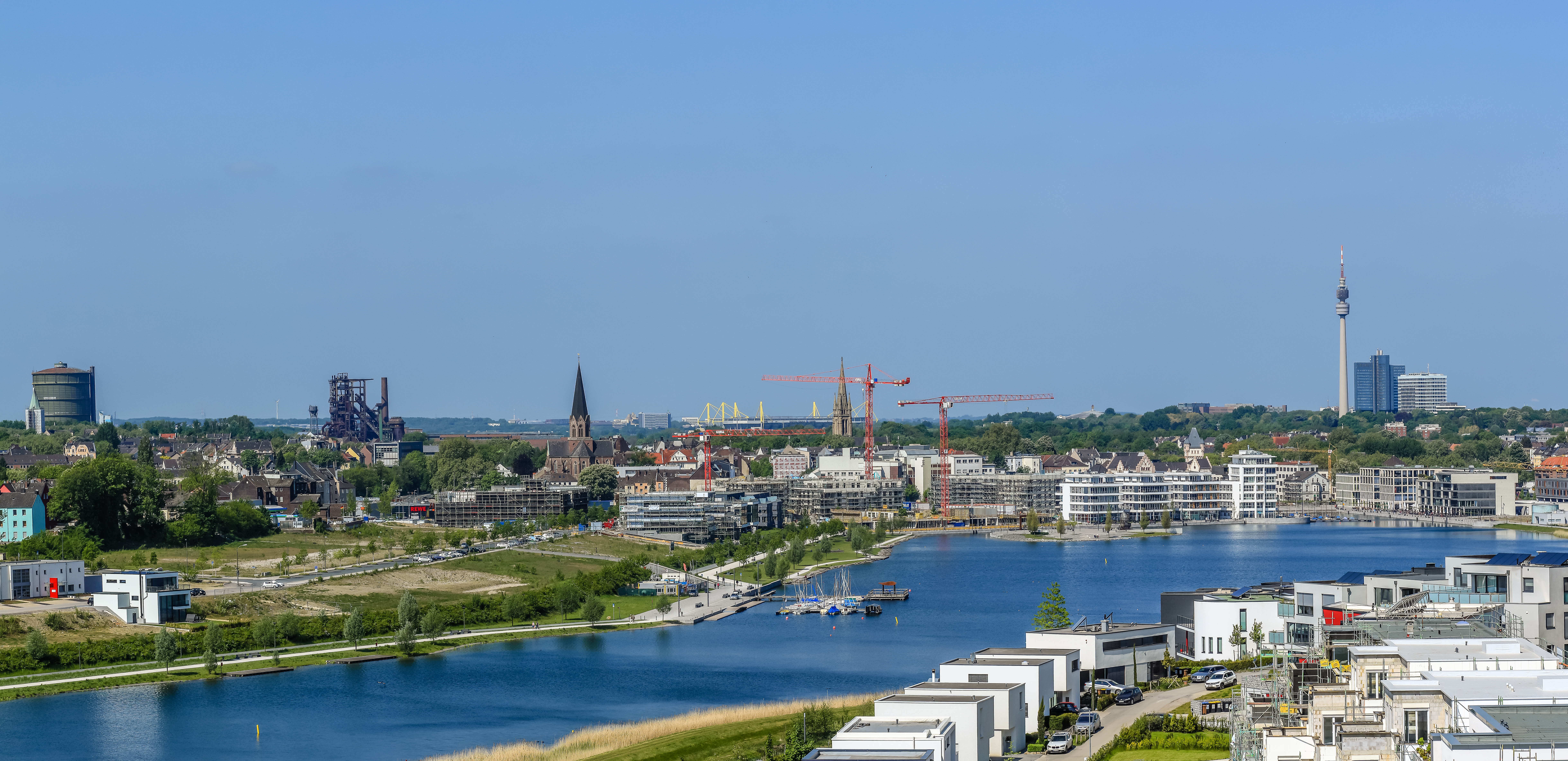 Wohnsiedlung am Wasser mit Blick auf Stadt, Fluss, moderne Häuser und Baukräne im Hintergrund.