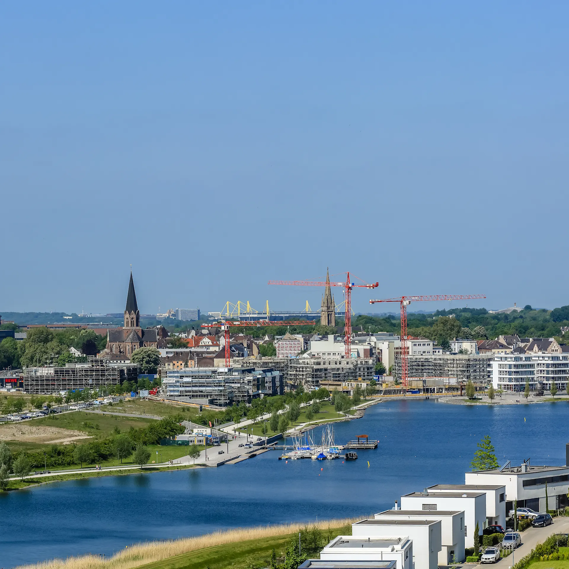 Wohnsiedlung am Wasser mit Blick auf Stadt, Fluss, moderne Häuser und Baukräne im Hintergrund.