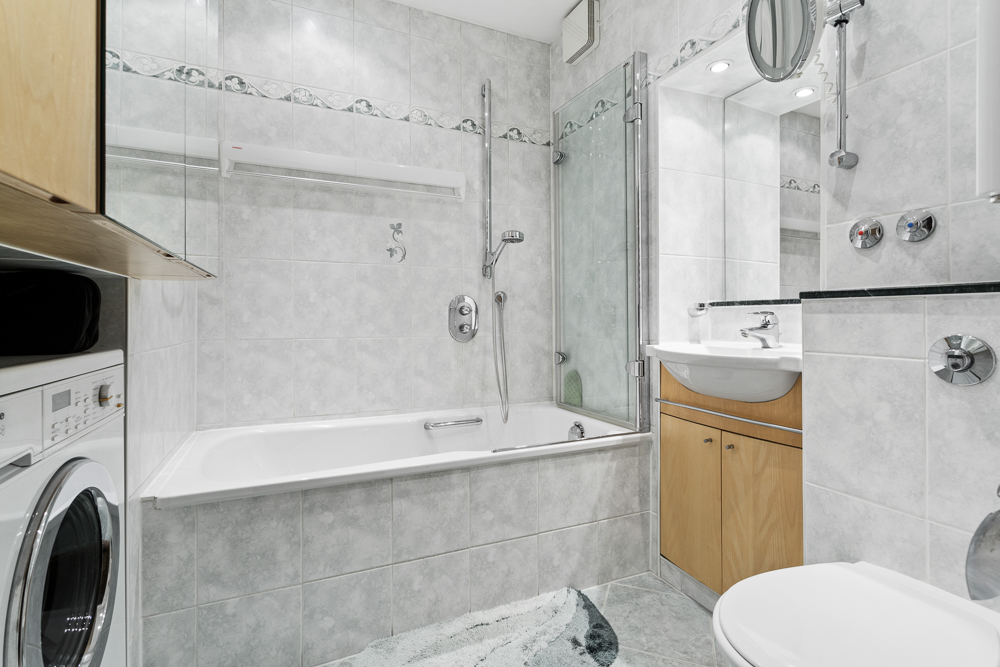 Helles Badezimmer mit Badewanne, Duschwand, Waschbecken, Waschmaschine und Toilette.