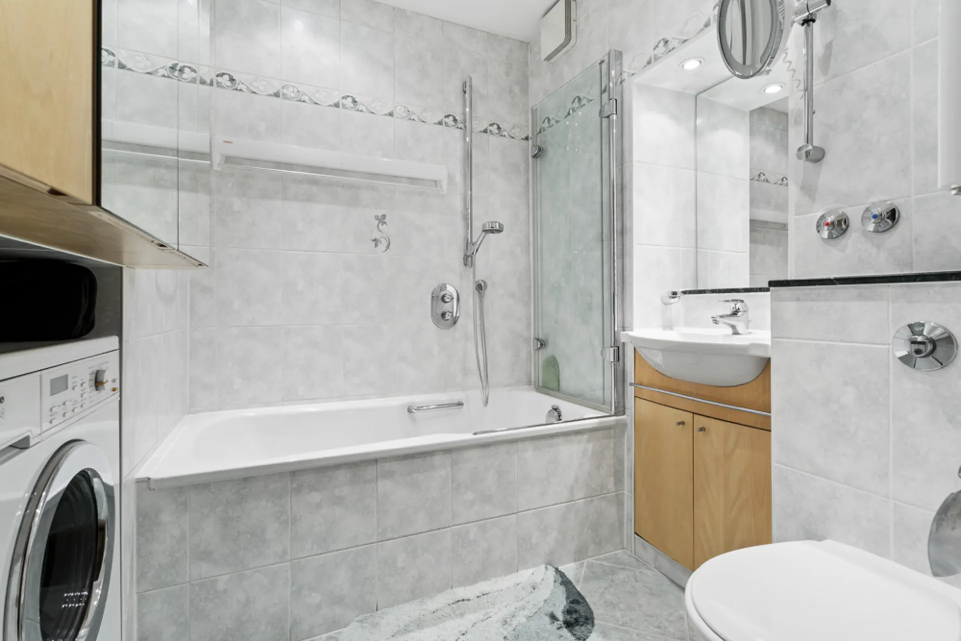 Helles Badezimmer mit Badewanne, Duschwand, Waschbecken, Waschmaschine und Toilette.