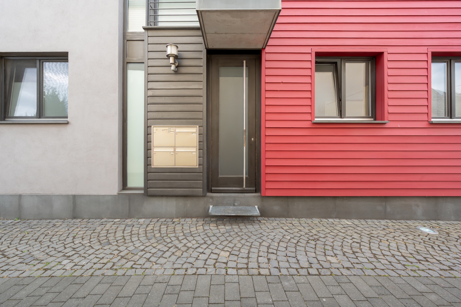 Moderne Hauseingangstür mit Briefkästen, zwei Fenstern und roter Holzfassade.