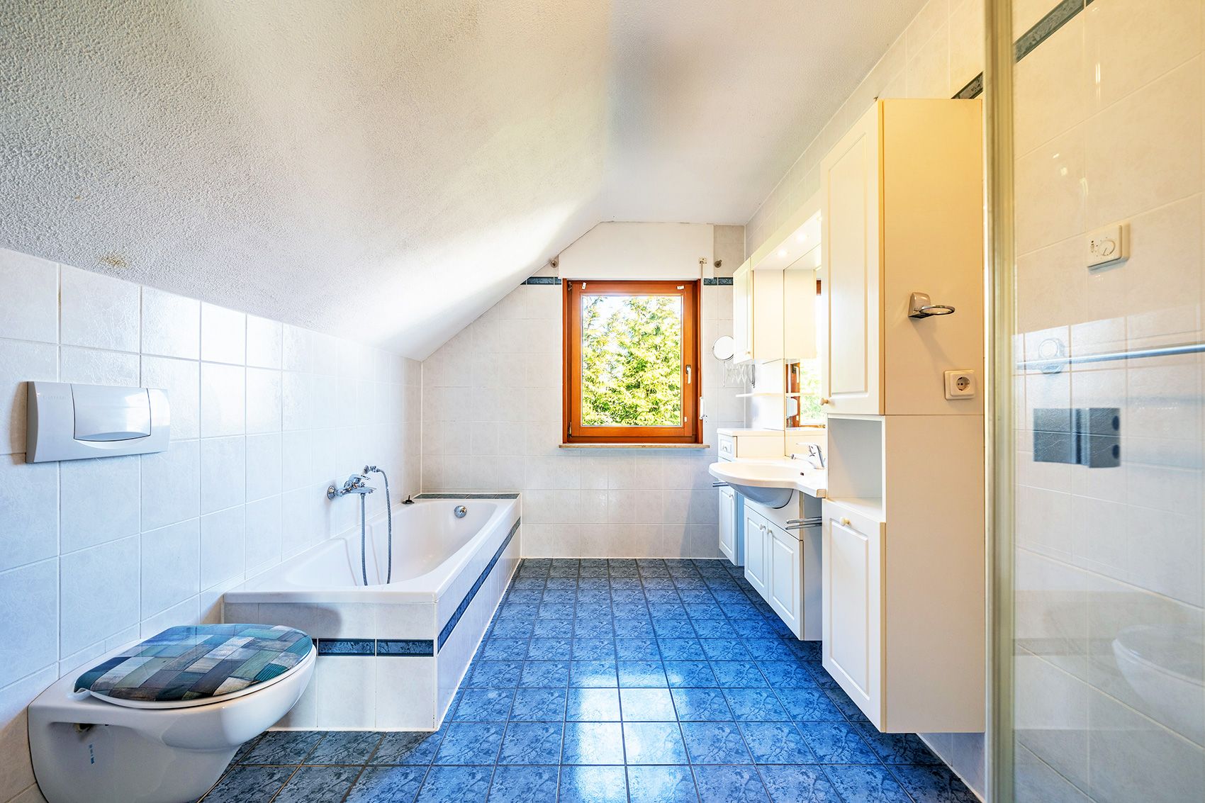 Helles Badezimmer mit Badewanne, Toilette, Waschbecken, Schränken und Fenster.