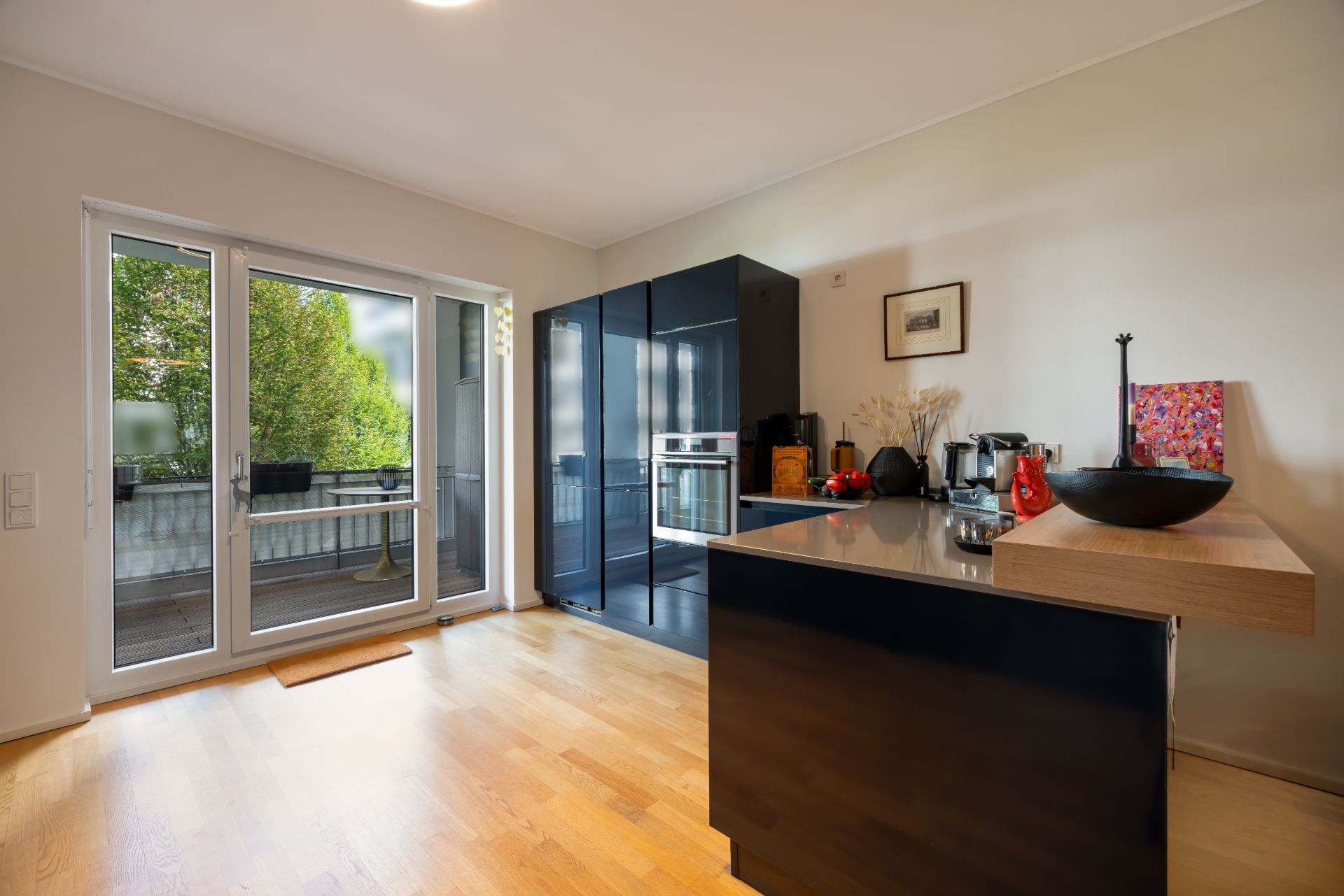 Moderne Küche mit dunklen Schränken, Holzfußboden und Zugang zu einem Balkon mit Glas-Tür.