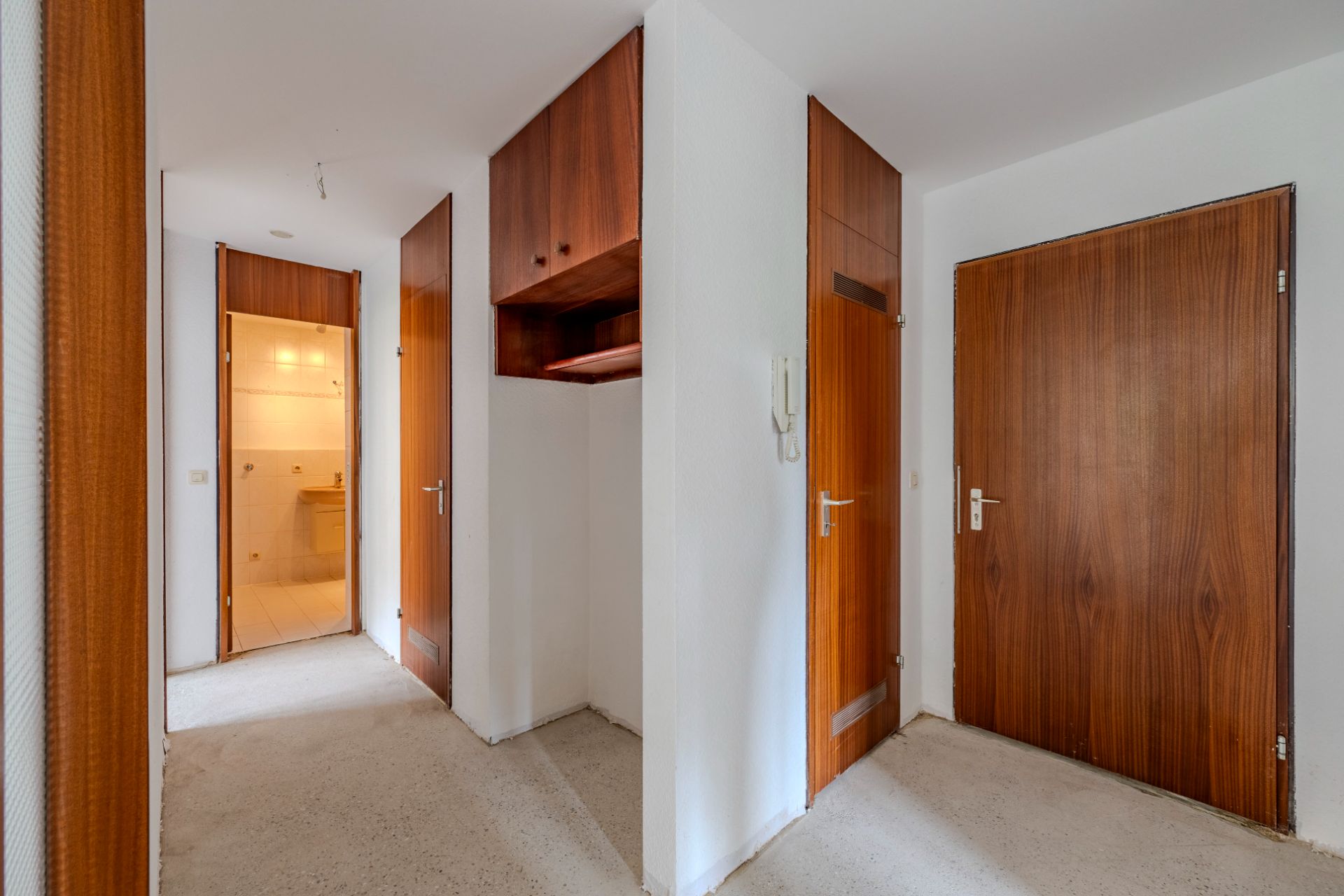 Flur mit Holztüren, Wandschrank und Blick ins beleuchtete Badezimmer.