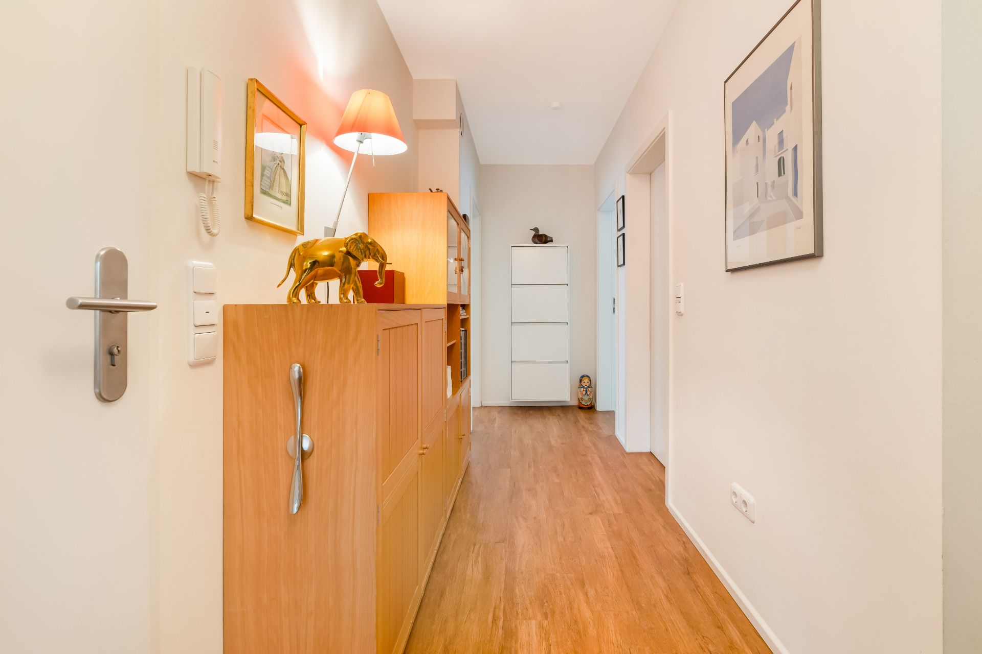 Heller Flur mit Holzschrank, Lampe, Dekorationen und Holzfußboden.