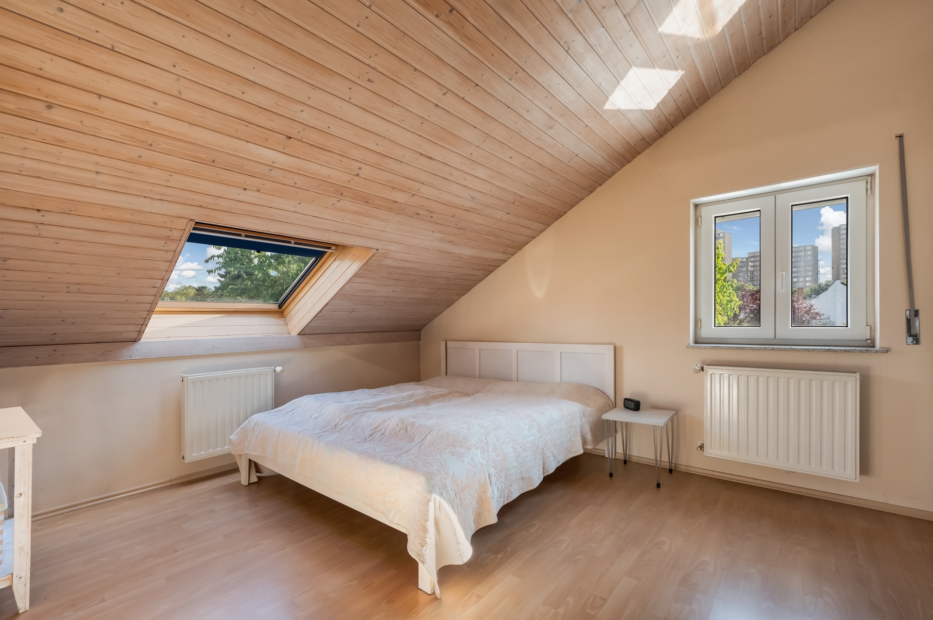 Helles Schlafzimmer mit Dachschräge, Doppelbett, Fenster und Holzdecke.