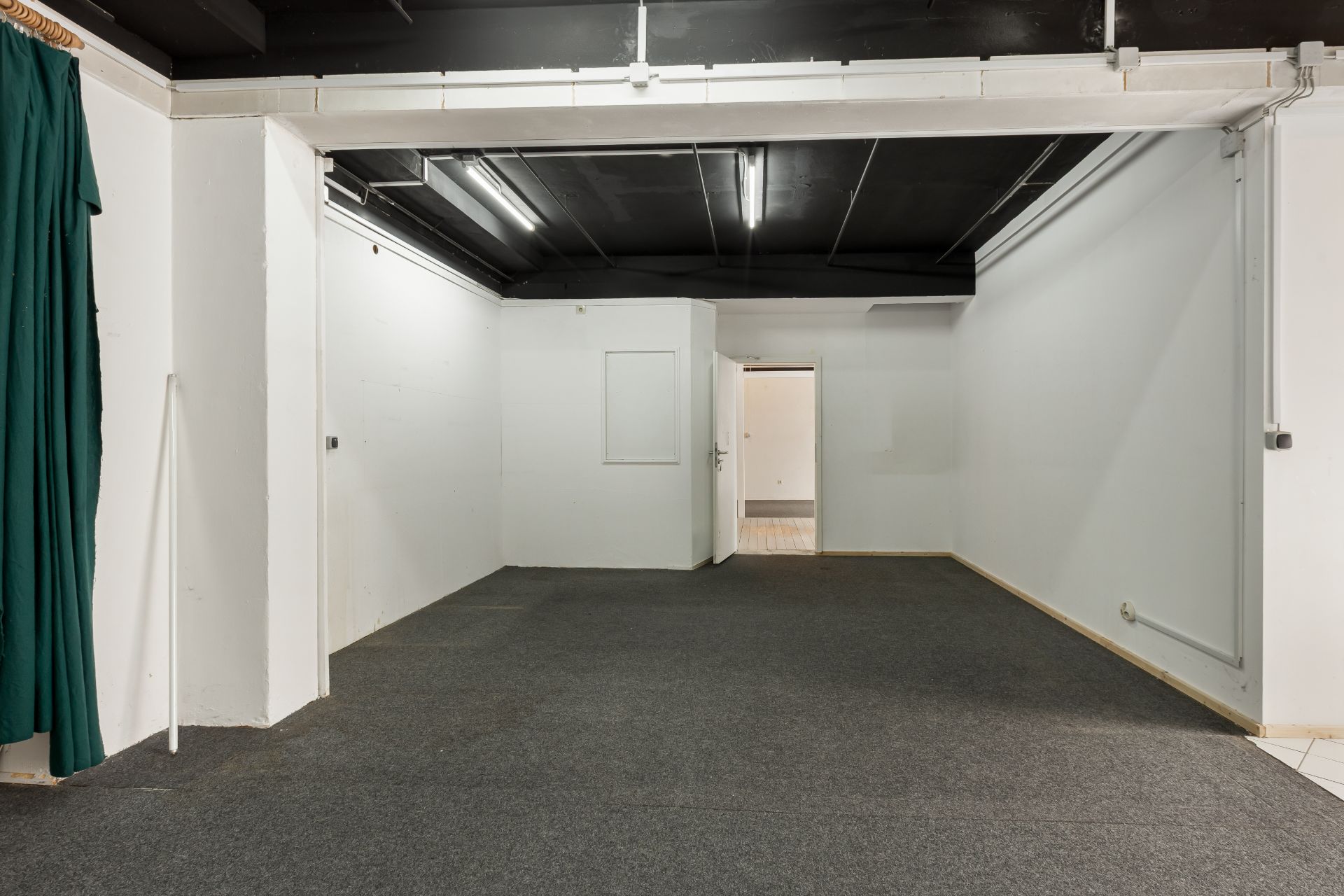 Ein leerer, rechteckiger Raum mit weiß gestrichenen Wänden und dunkler Decke, grauer Teppichboden.