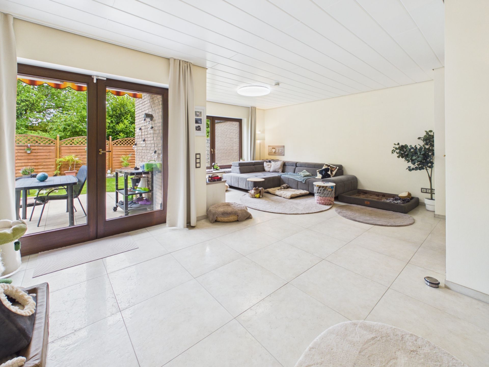 Helles Wohnzimmer mit großer Eckcouch, Esstisch am Fenster und Zugang zur Terrasse mit Garten.