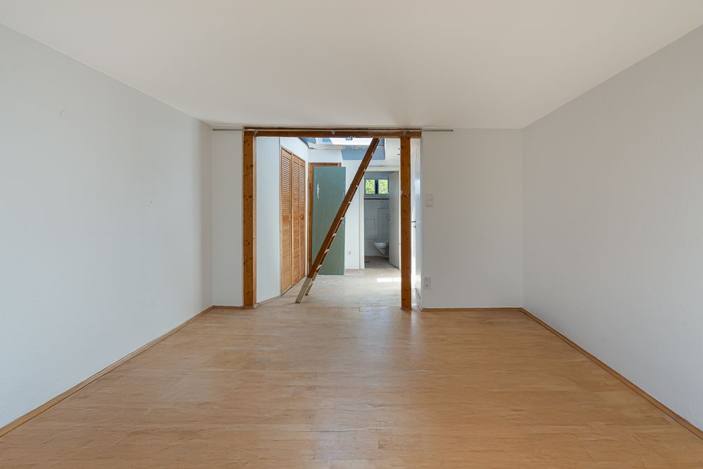 Leerer Raum mit hellem Holzboden und offener Tür zu einem weiteren Zimmer.