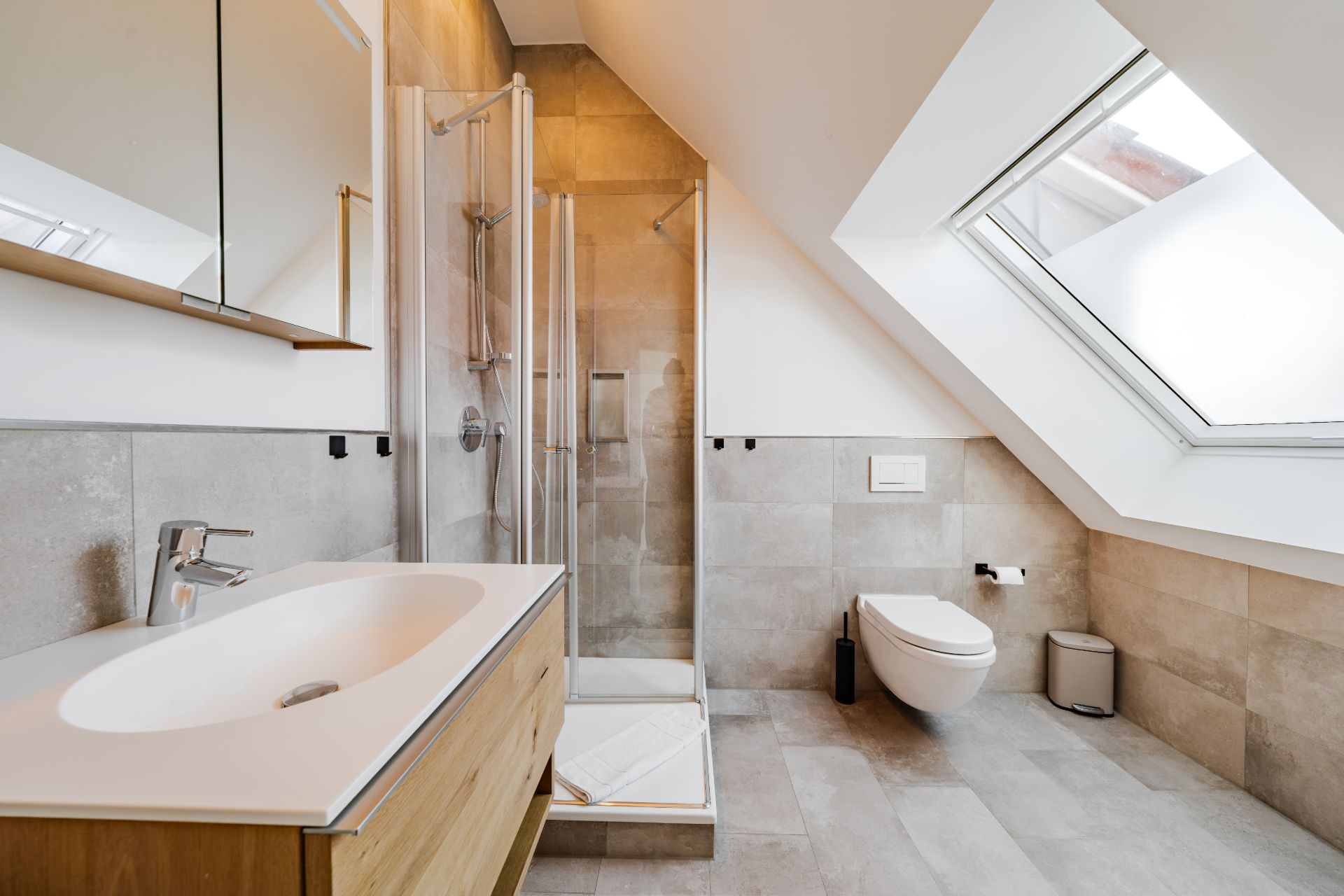 Modernes Bad mit Waschbecken, Dusche, WC und großem Dachfenster.