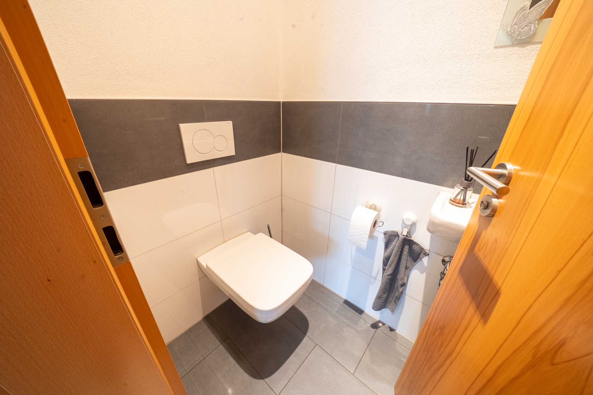 Kleines modernes WC mit Wandtoilette, Waschbecken, Handtuch und Toilettenpapierrolle.