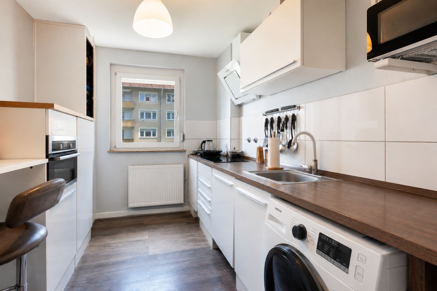 Moderne Küche mit Holzarbeitsplatte, Waschmaschine, Spüle und Fenster mit Blick auf Wohnhäuser.