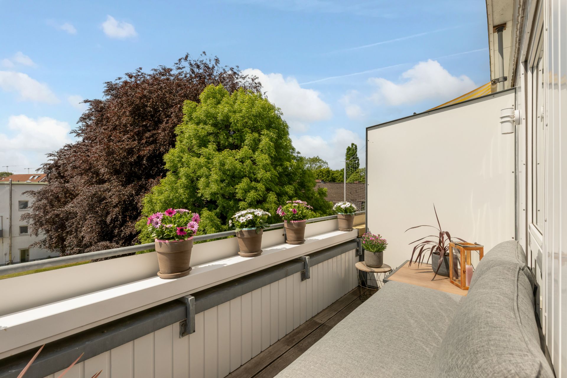 Balkon mit Blumenkästen, Bank und Blick auf grüne Bäume.