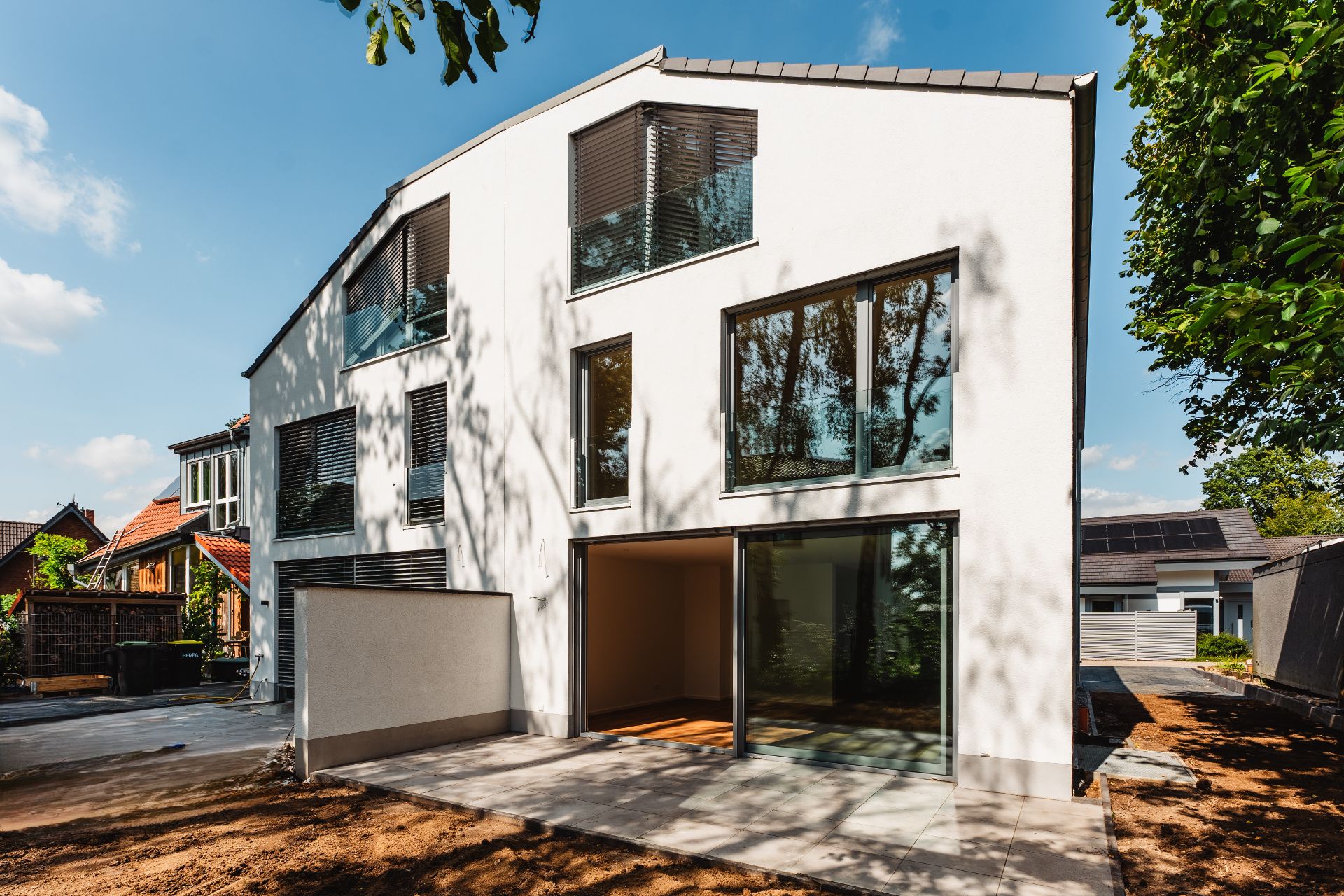 Modernes, weißes Wohnhaus mit großen Fenstern und Terrasse, umgeben von Bäumen.