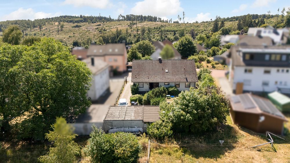 Luftaufnahme eines Einfamilienhauses mit Garten, Nebengebäude und umliegenden Bäumen.