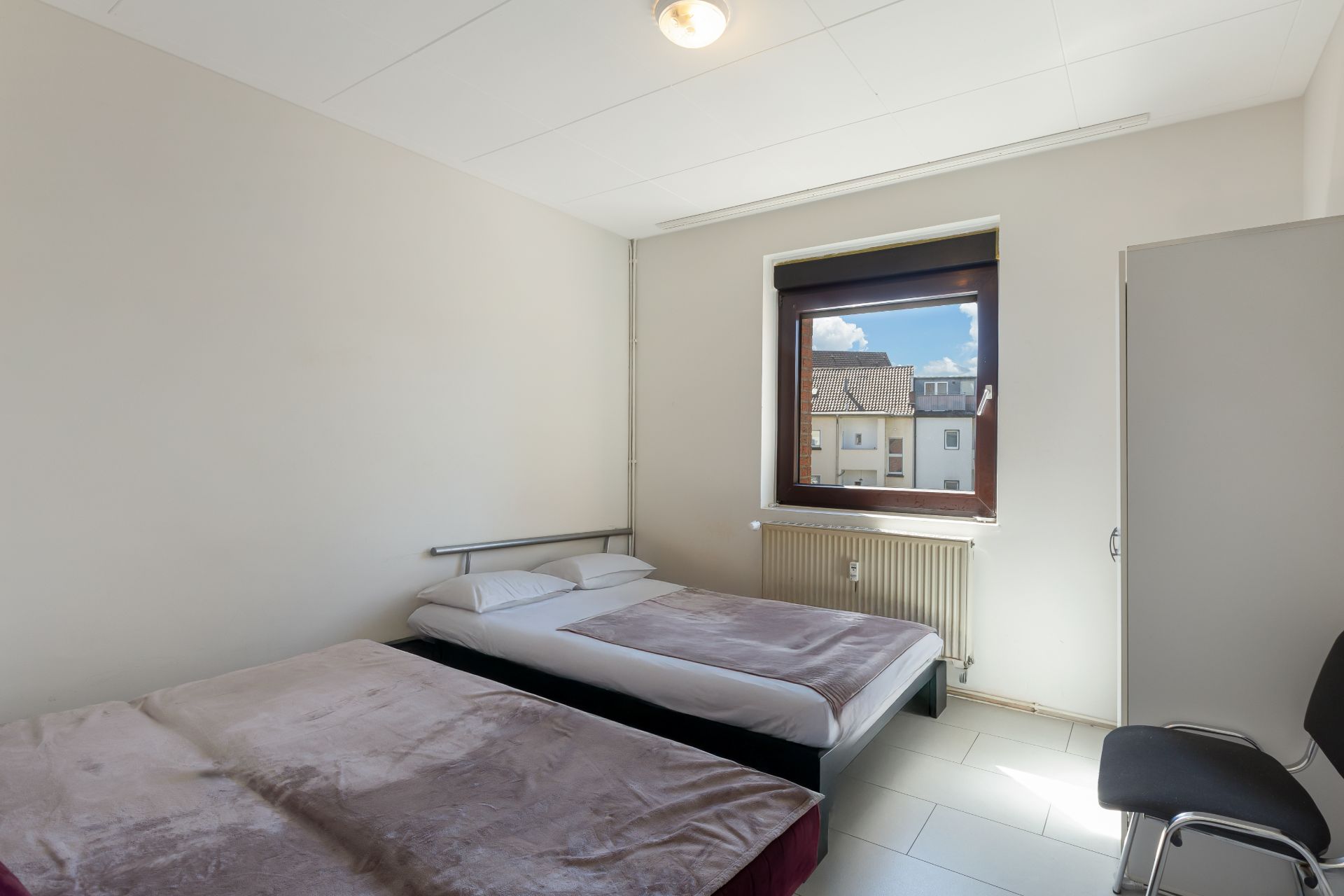 Schlafzimmer mit zwei Betten, einem Fenster, einem Schrank und einem Stuhl.