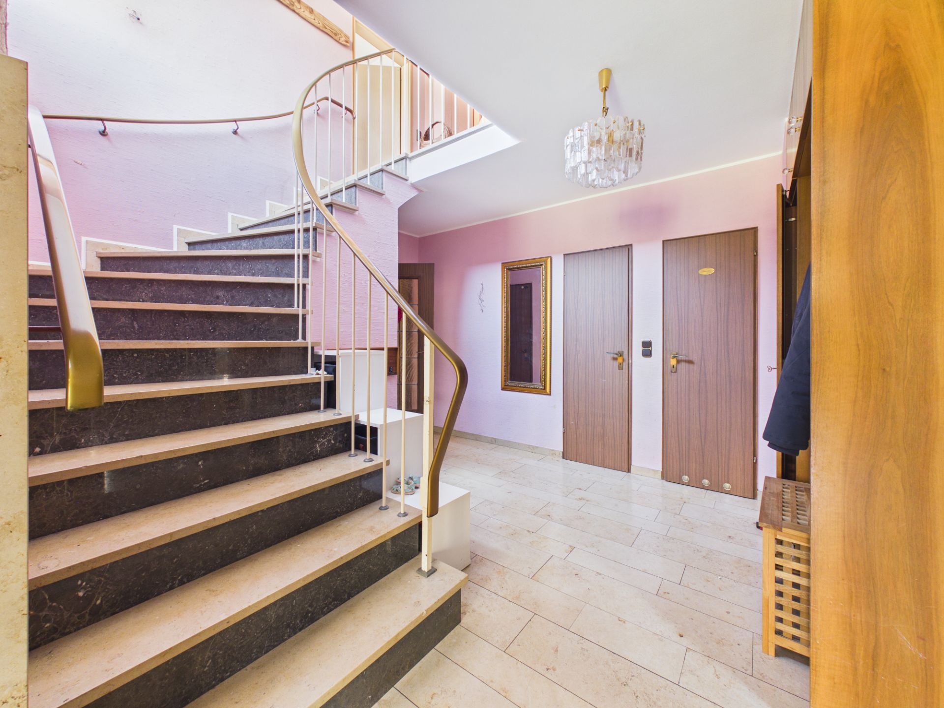 Heller Flur mit Marmortreppe, zwei Holztüren und Kronleuchter.