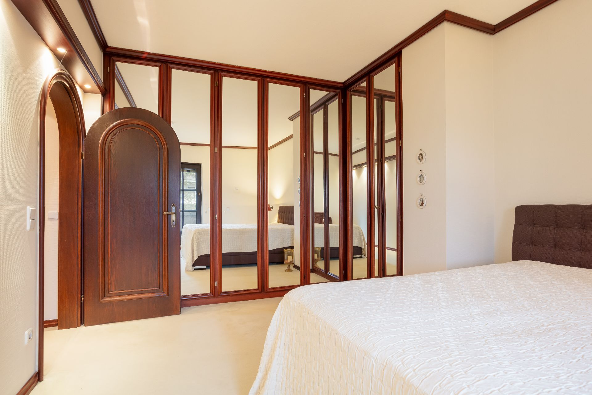 Schlafzimmer mit großem Spiegel-Kleiderschrank, Holztür und beige Bettdecke.