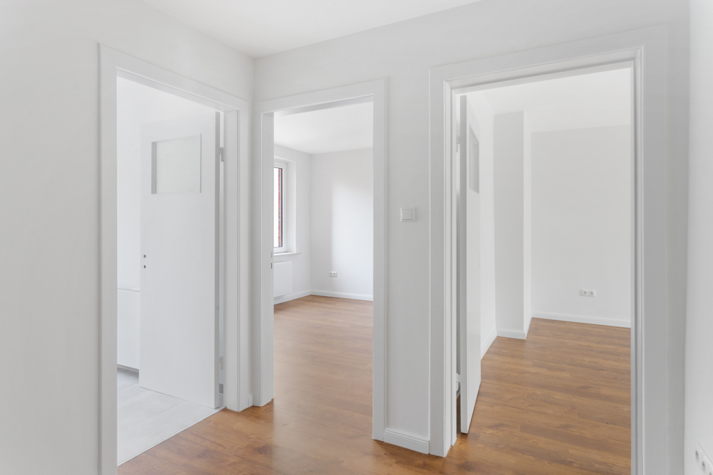 Heller Flur mit drei offenen Türen, Holzboden und weißen Wänden in einer Wohnung.