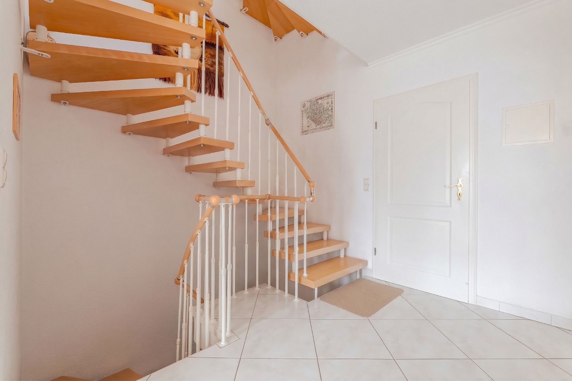Helle Diele mit Holztreppe und weißer Tür, gefliestem Boden und weiß gestrichenen Wänden.