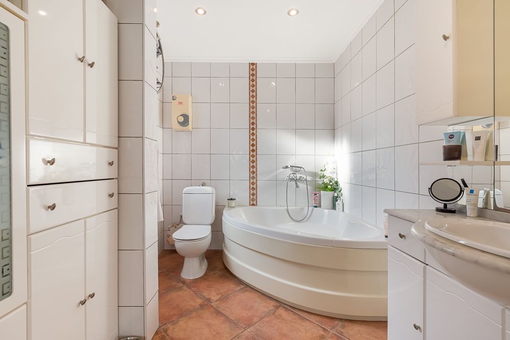 Helles Badezimmer mit Eckbadewanne, Toilette, Waschbecken und weißen Schränken.
