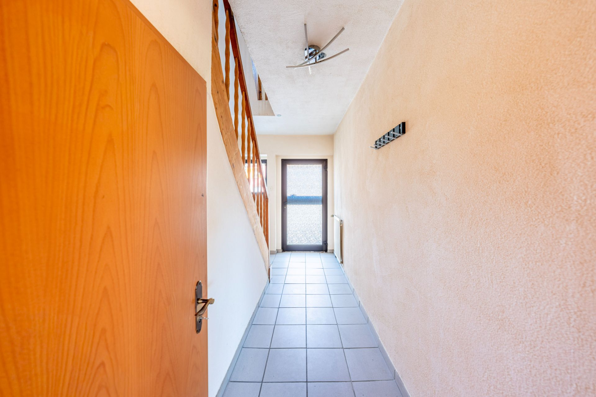 Heller Flur mit Fliesenboden, Holztür links, Treppe rechts und Glastür am Ende.