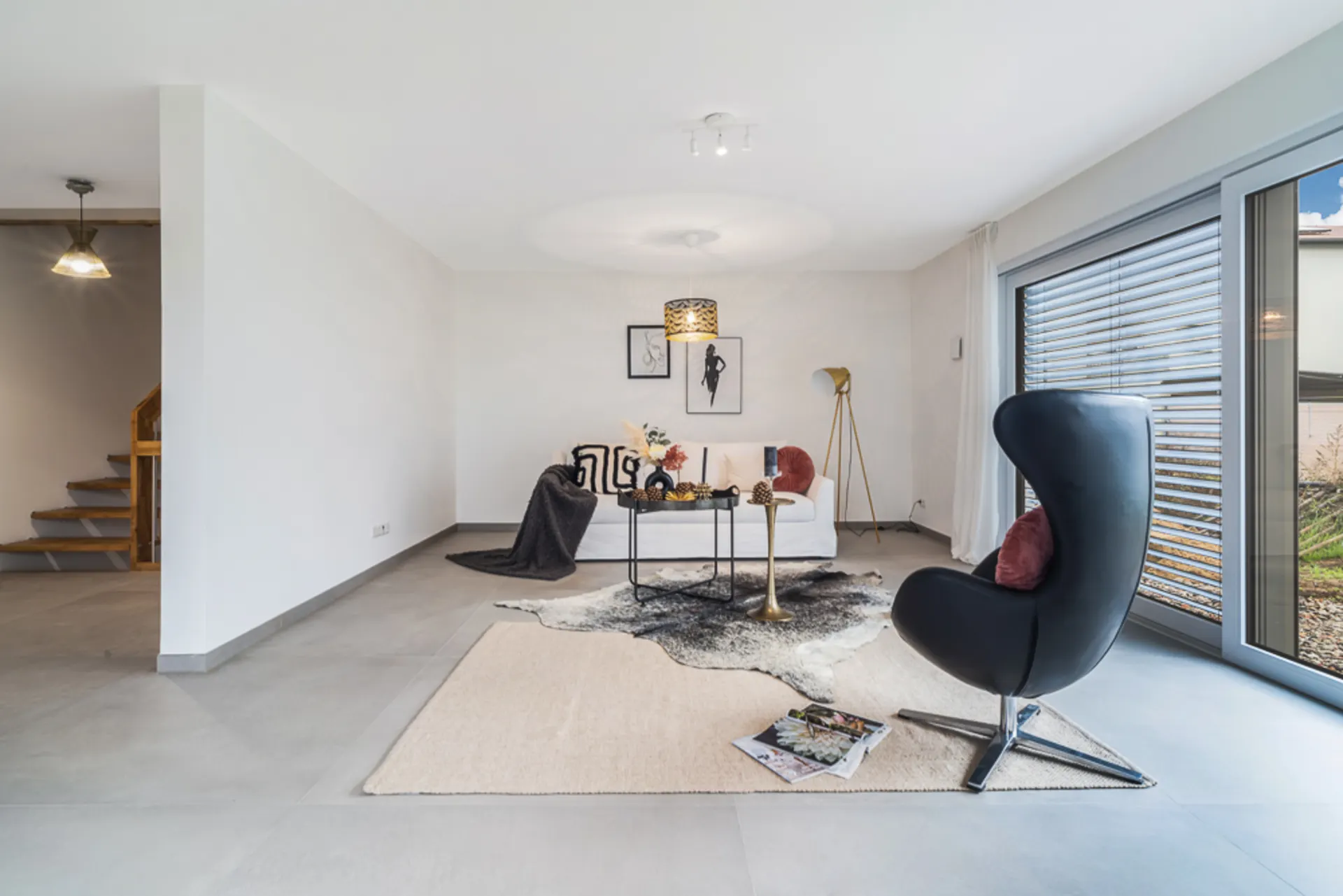 Modernes Wohnzimmer mit Sessel, Sofa, Couchtisch und großem Fenster mit Jalousien.