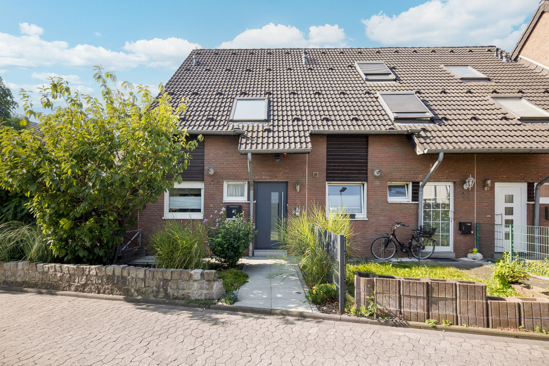 Zweistöckiges Reihenhaus mit Vorgarten, Fahrrädern und gepflastertem Weg zur Haustür.