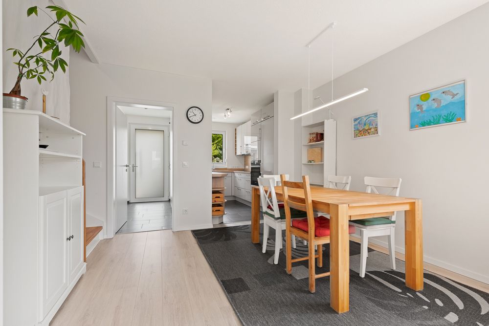 Essbereich mit Holztisch und vier Stühlen, neben einer offenen Küche in einer hellen Wohnung.