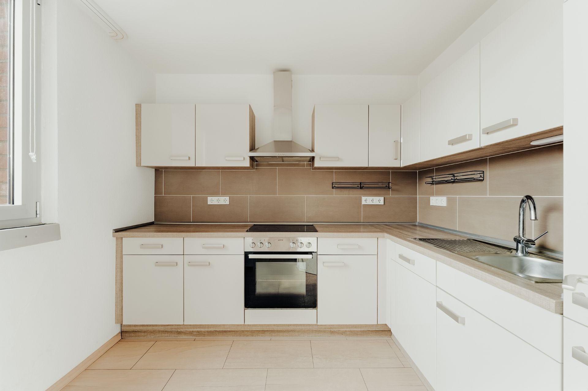 Moderne Einbauküche mit weißem Schränken, Herd, Backofen und Edelstahlspüle.