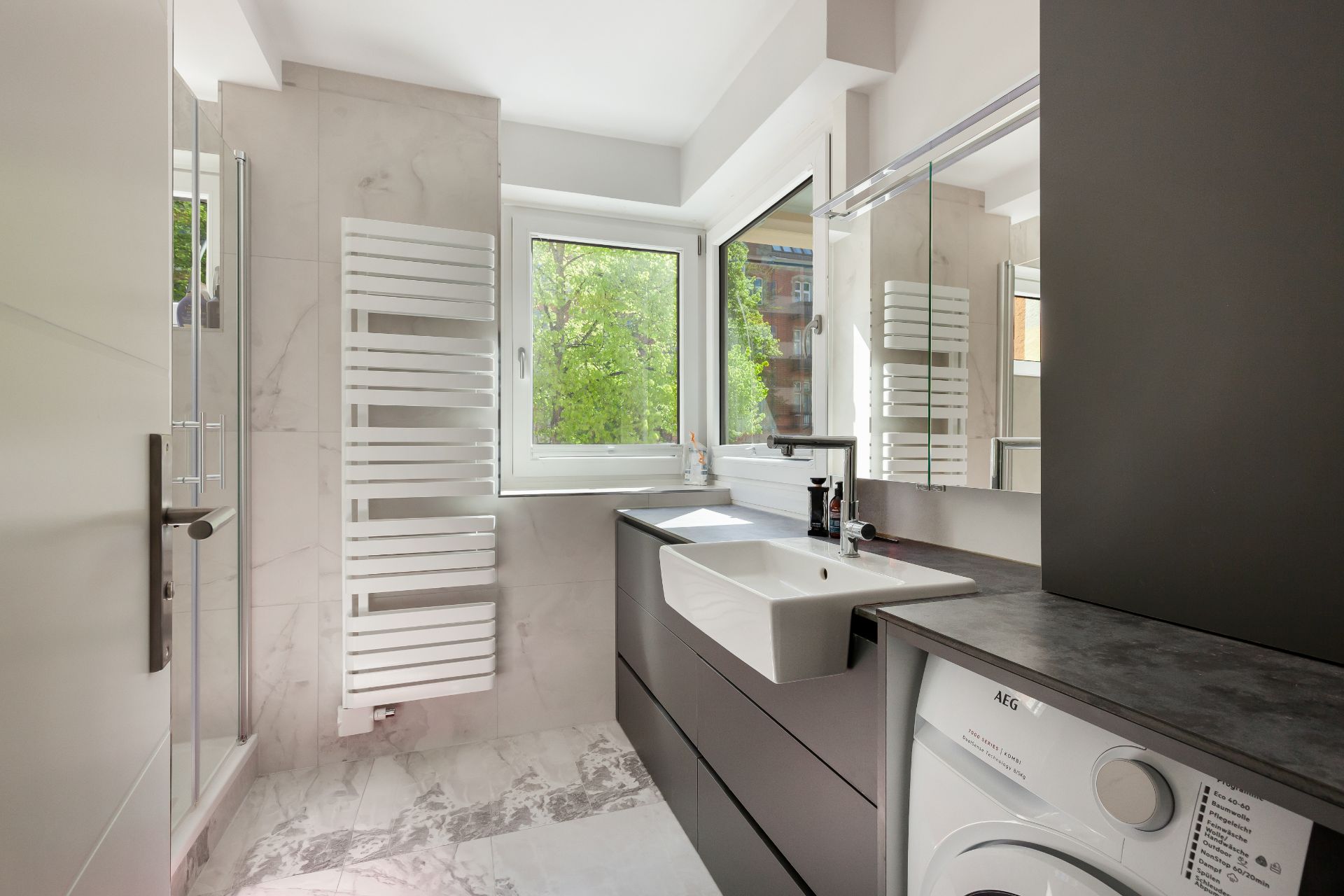 Modernes Badezimmer mit Waschbecken, Duschkabine, Fenster, Spiegel und Waschmaschine.