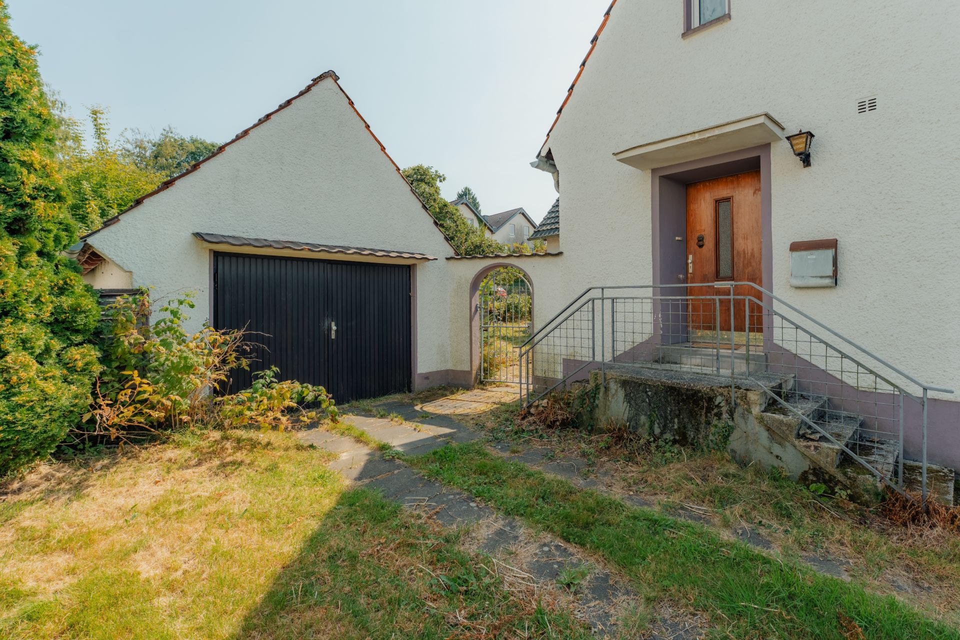 Eingang eines Wohnhauses mit Stufen, Garten und Garage mit Tor.