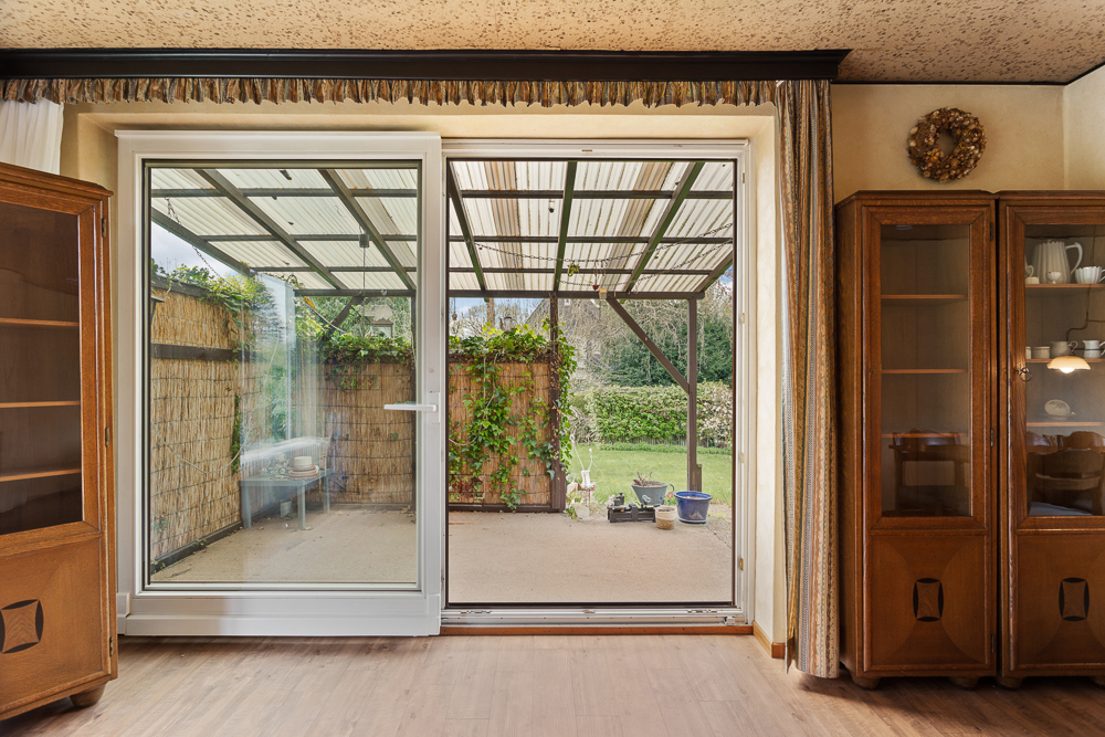 Wohnzimmer mit Glastür zur überdachten Terrasse und Blick auf Garten.