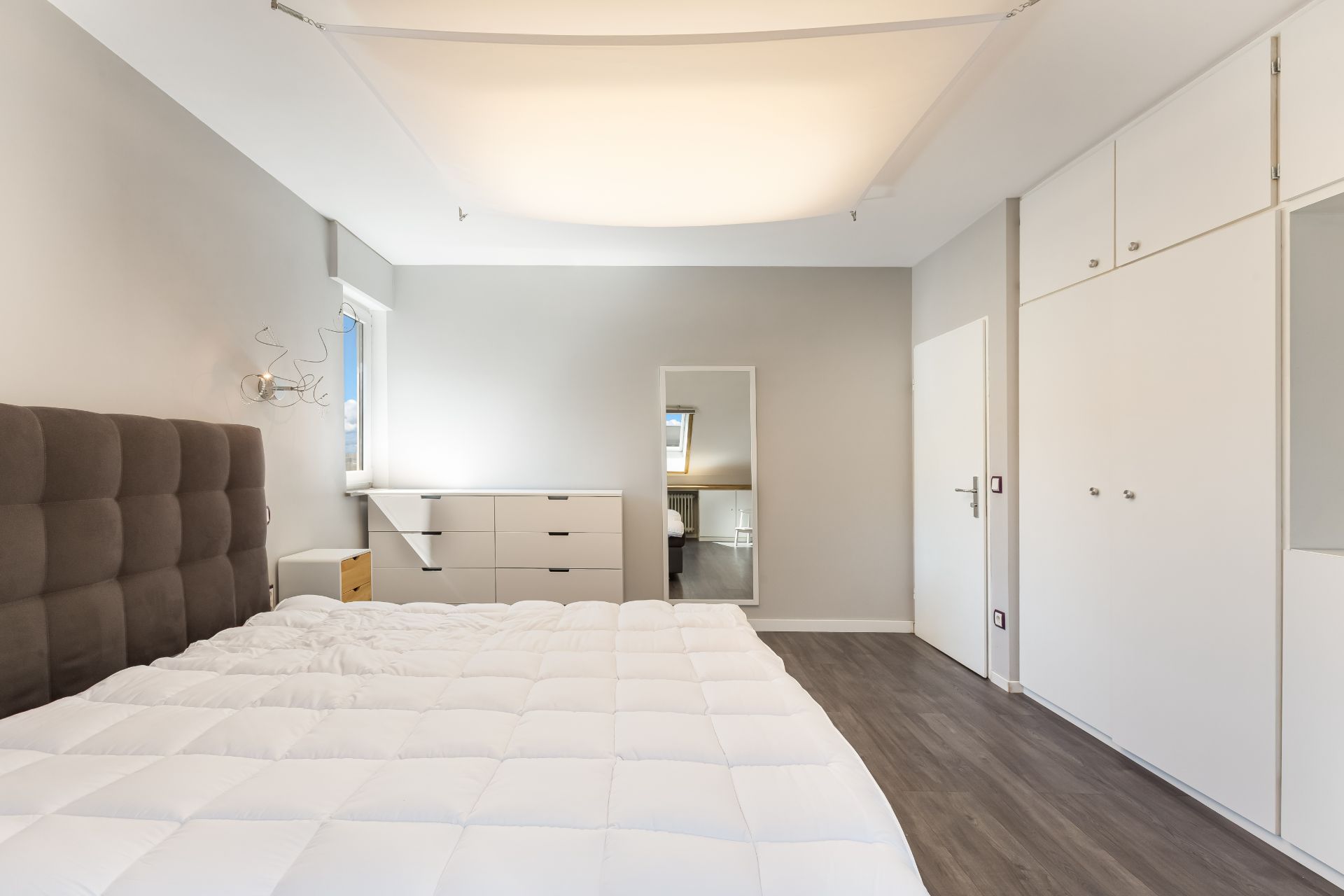 Helles Schlafzimmer mit großem Bett, Spiegel, Kommode und weißem Wandschrank.