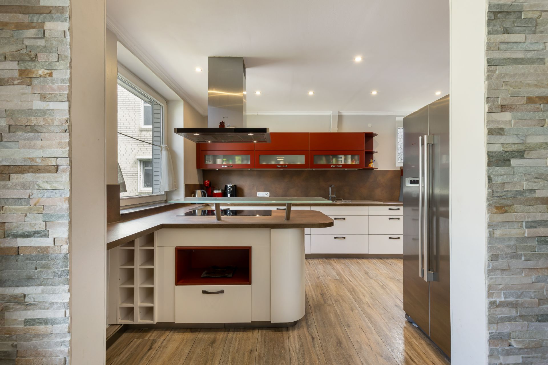 Moderne Wohnküche mit Kücheninsel, roten Oberschränken und großem Kühlschrank.