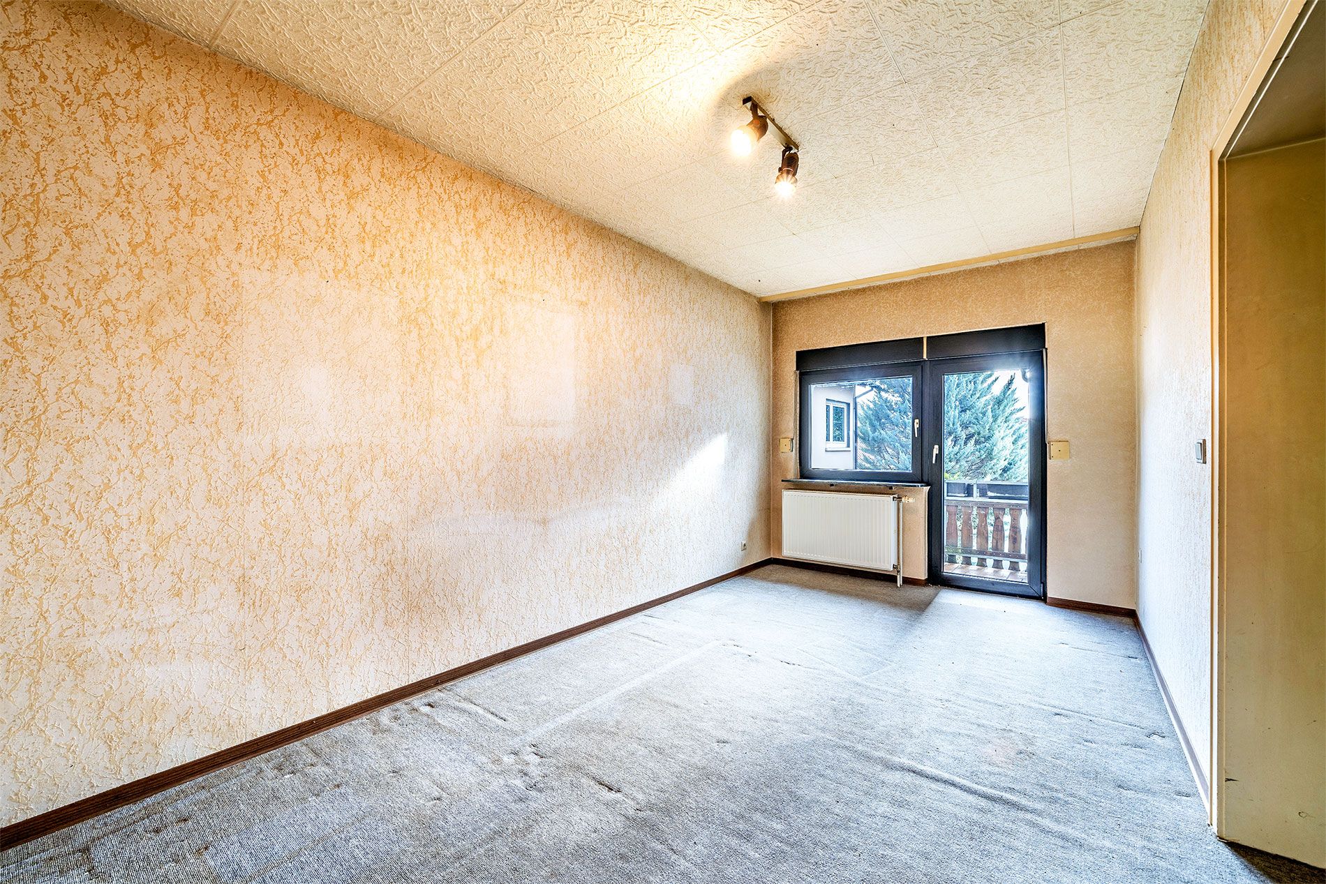 Leerer Raum mit Teppichboden, hellen Wänden und Fenster mit Zugang zu einem kleinen Balkon.