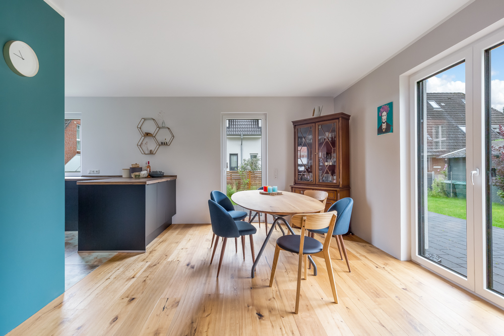 Helles Esszimmer mit rundem Holztisch, vier Stühlen, Vitrine und Zugang zur Terrasse.