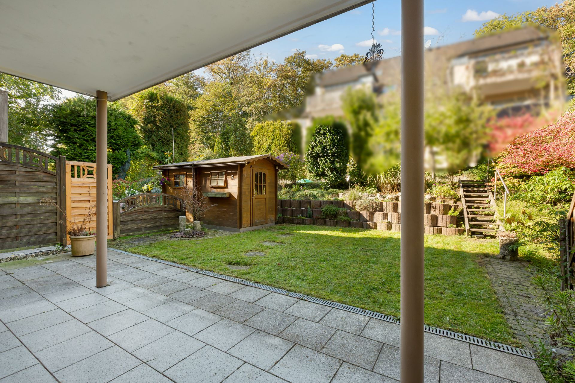 Überdachte Terrasse mit Blick auf Garten, Rasenfläche und Holzhaus.
