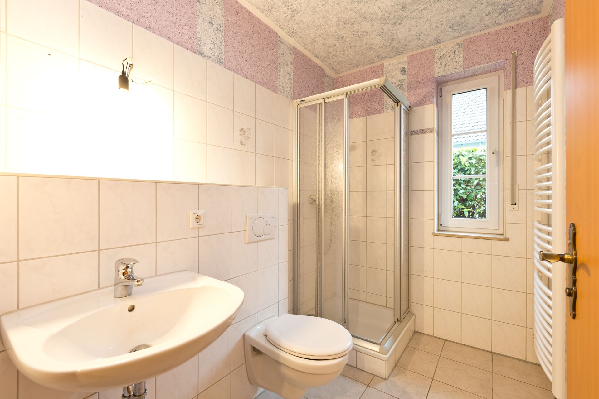Helles Bad mit Waschbecken, Dusche, WC, Handtuchheizkörper und Fenster.