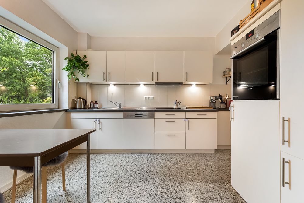 Moderne, helle Einbauküche mit großem Fenster, weißen Schränken und Esstisch.