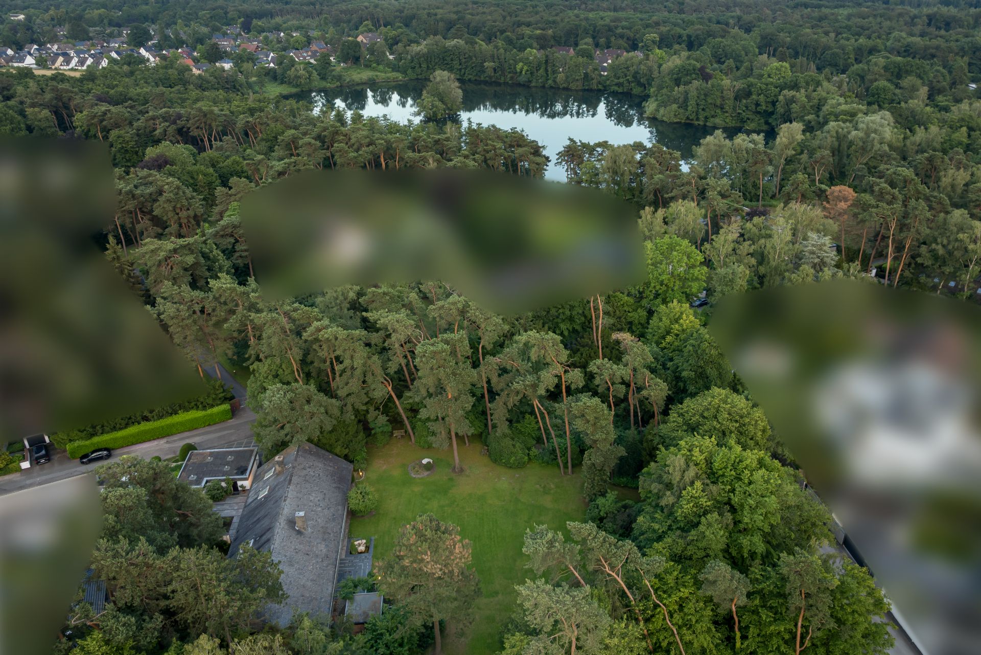 Luftaufnahme eines Hauses mit großem Garten und Bäumen neben einem See.