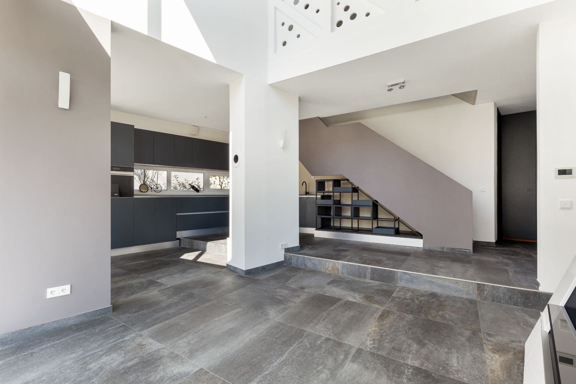Modernes Wohninnere mit grauen Fliesen, offener Küche und Treppe mit Stauraum.