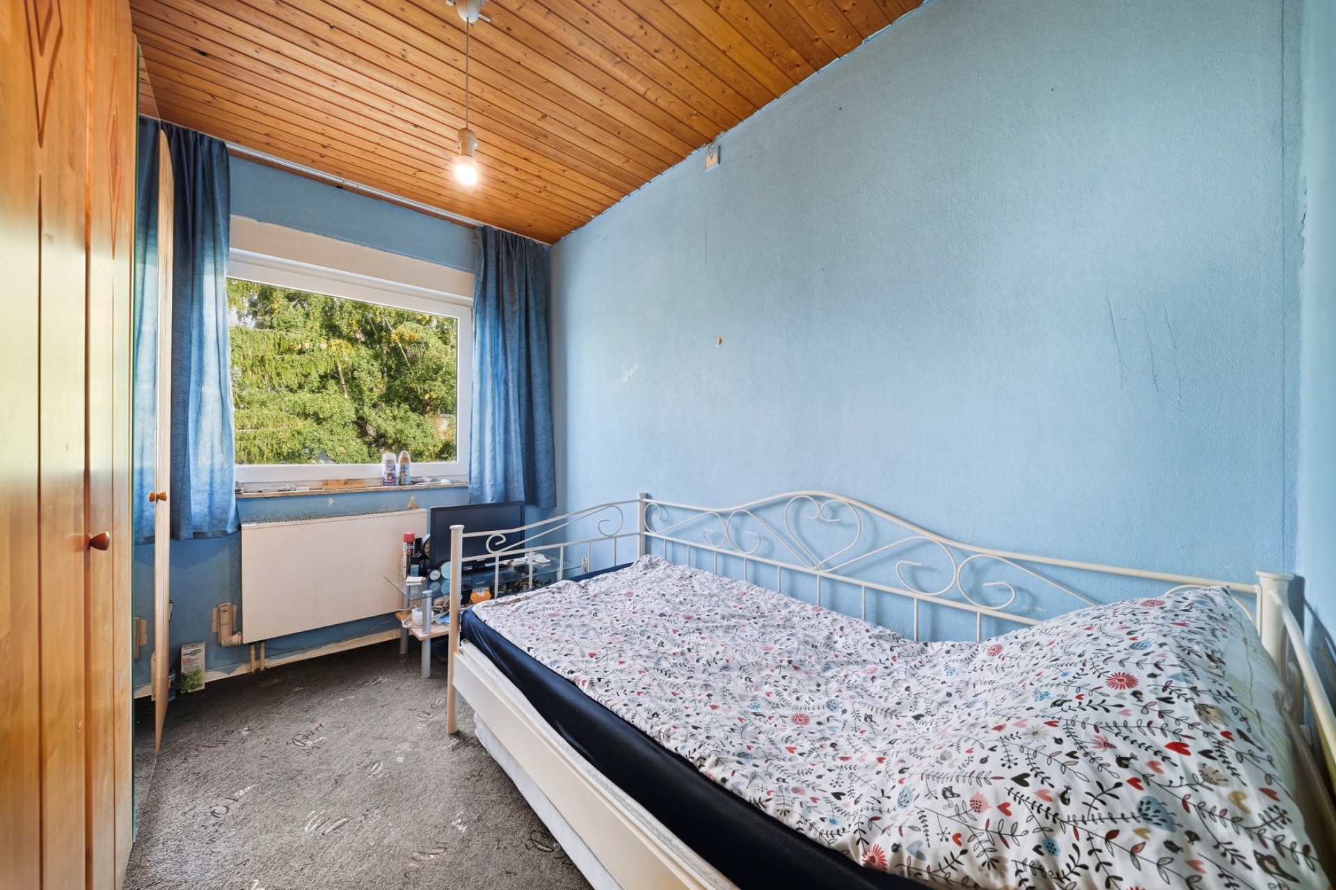 Kleines Schlafzimmer mit Bett, Fenster, blauen Wänden und Holzdecke.