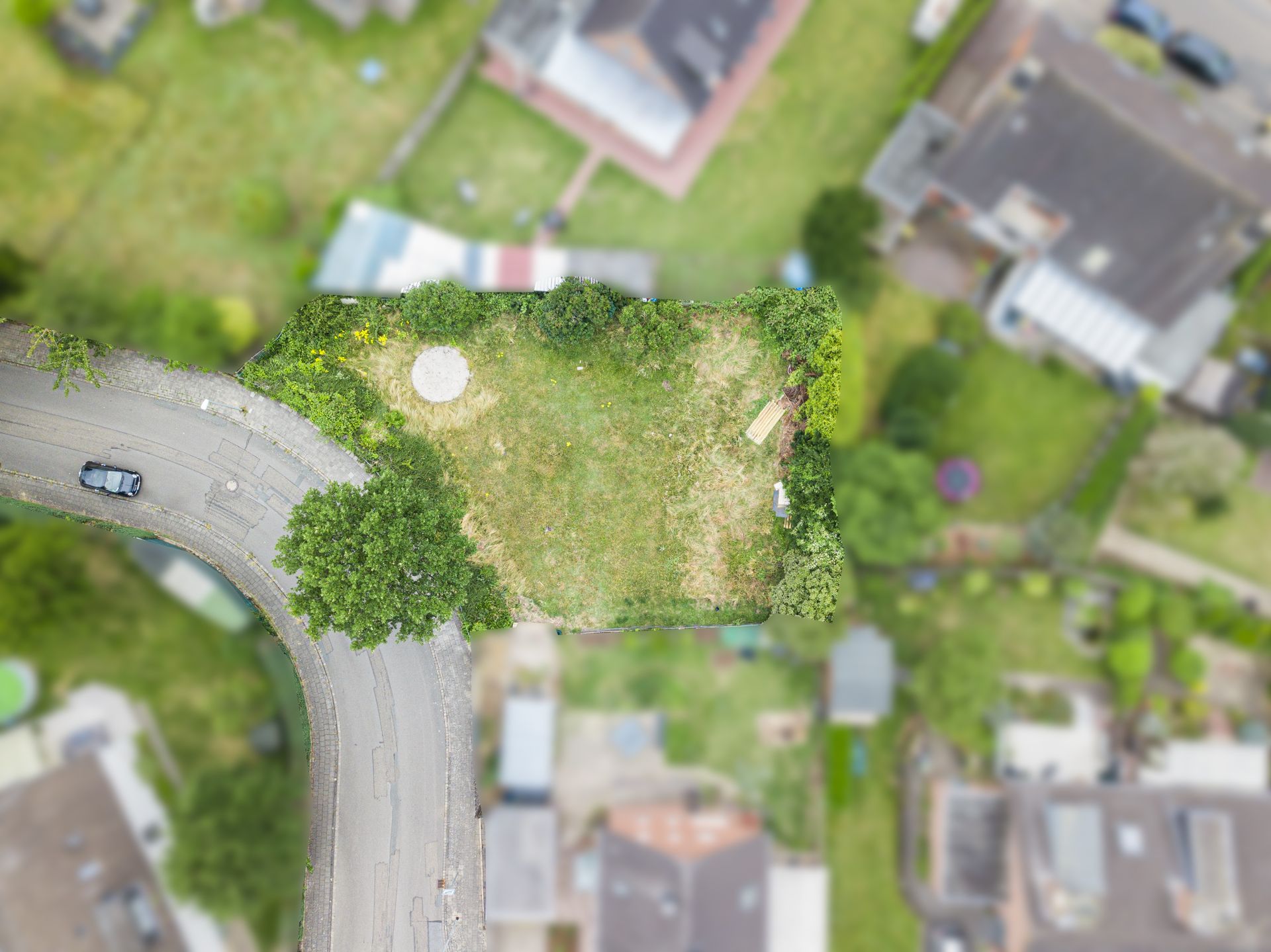 Luftaufnahme eines umzäunten Gartengrundstücks mit Rasen, Baum und runder Fläche.