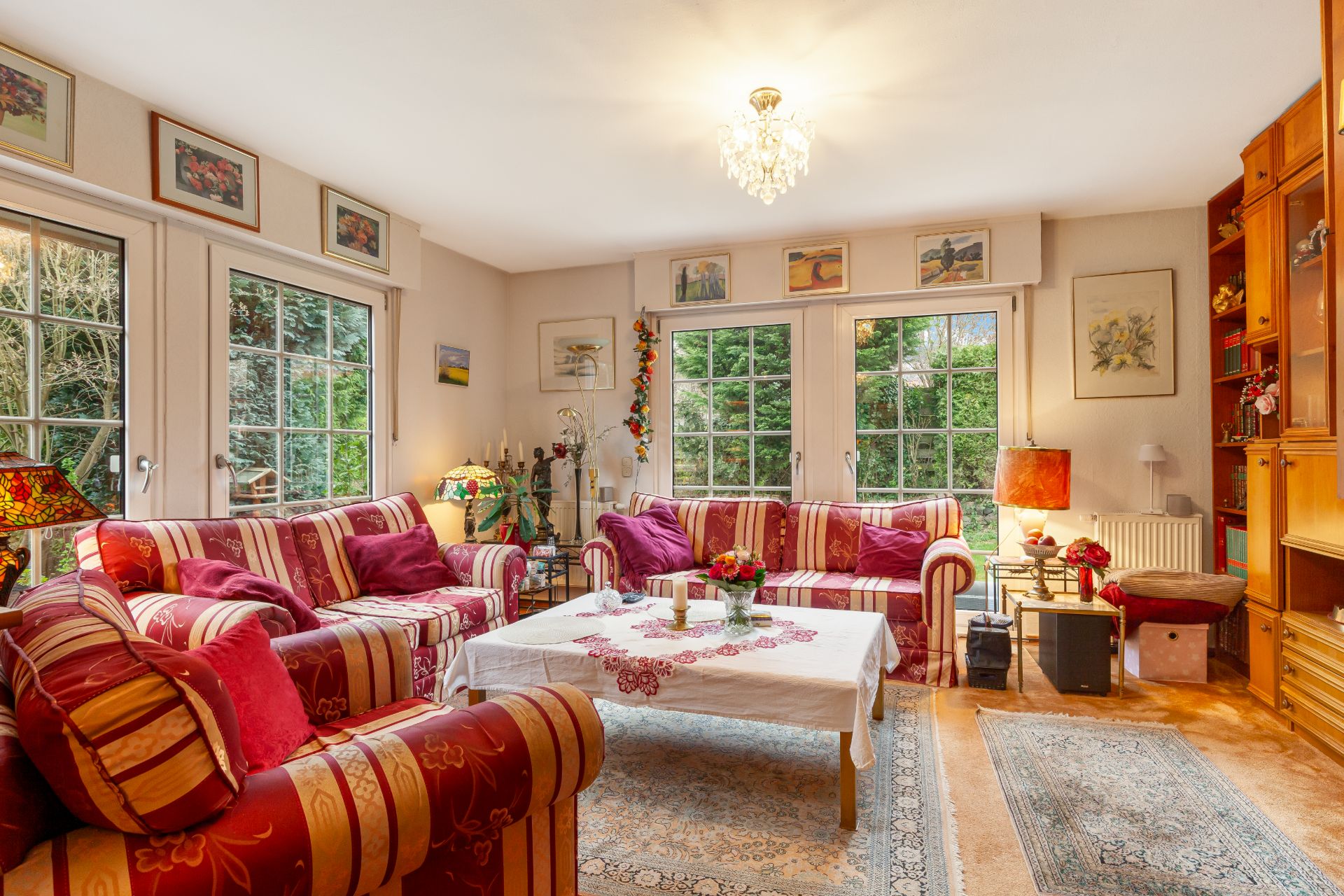 Helles Wohnzimmer mit gemusterten Sofas, Couchtisch, Teppichen und Fenstern mit Blick auf den Garten.