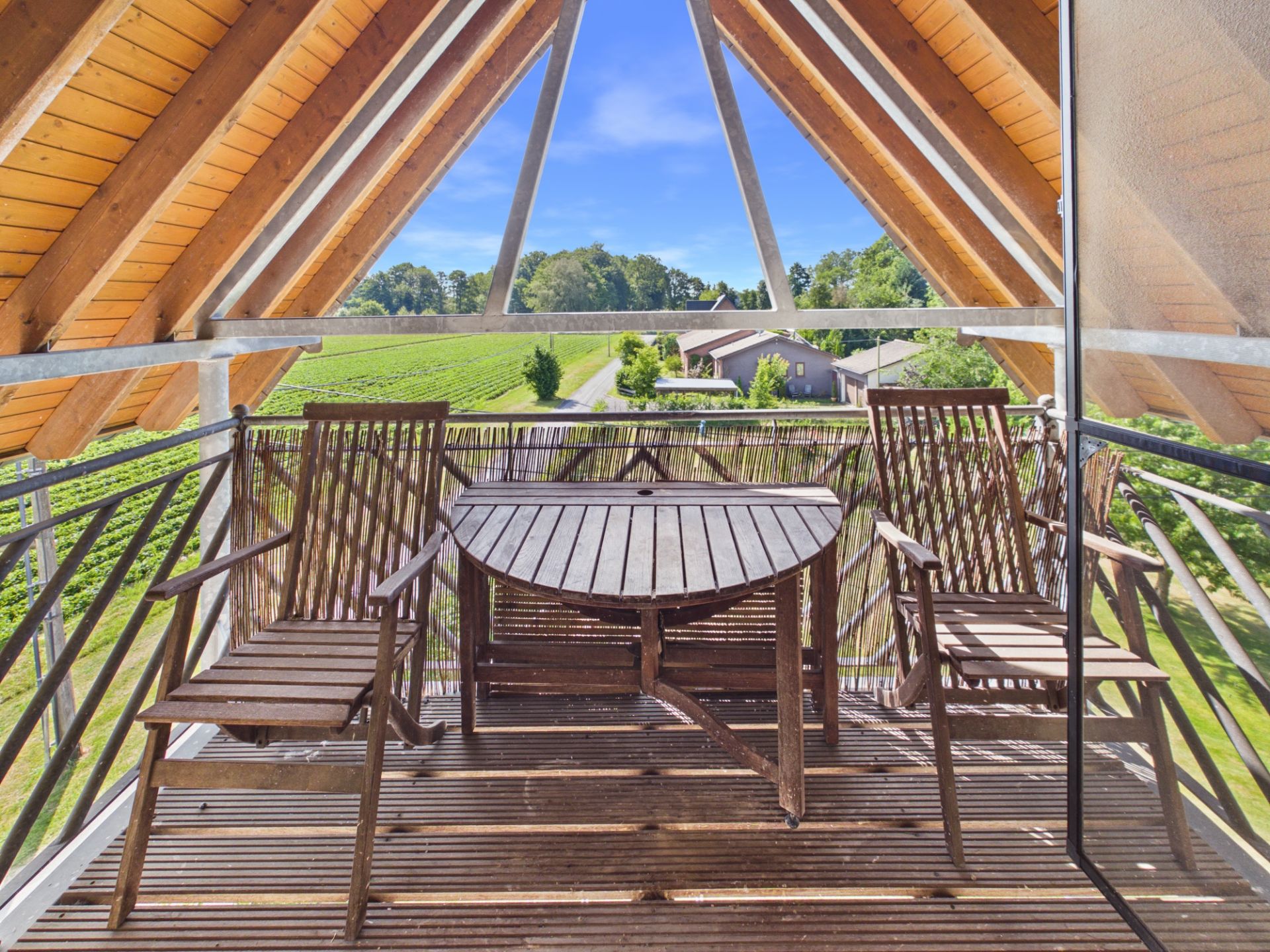 Holzbalkon mit zwei Stühlen und einem Tisch, Blick auf grüne Landschaft und Häuser.