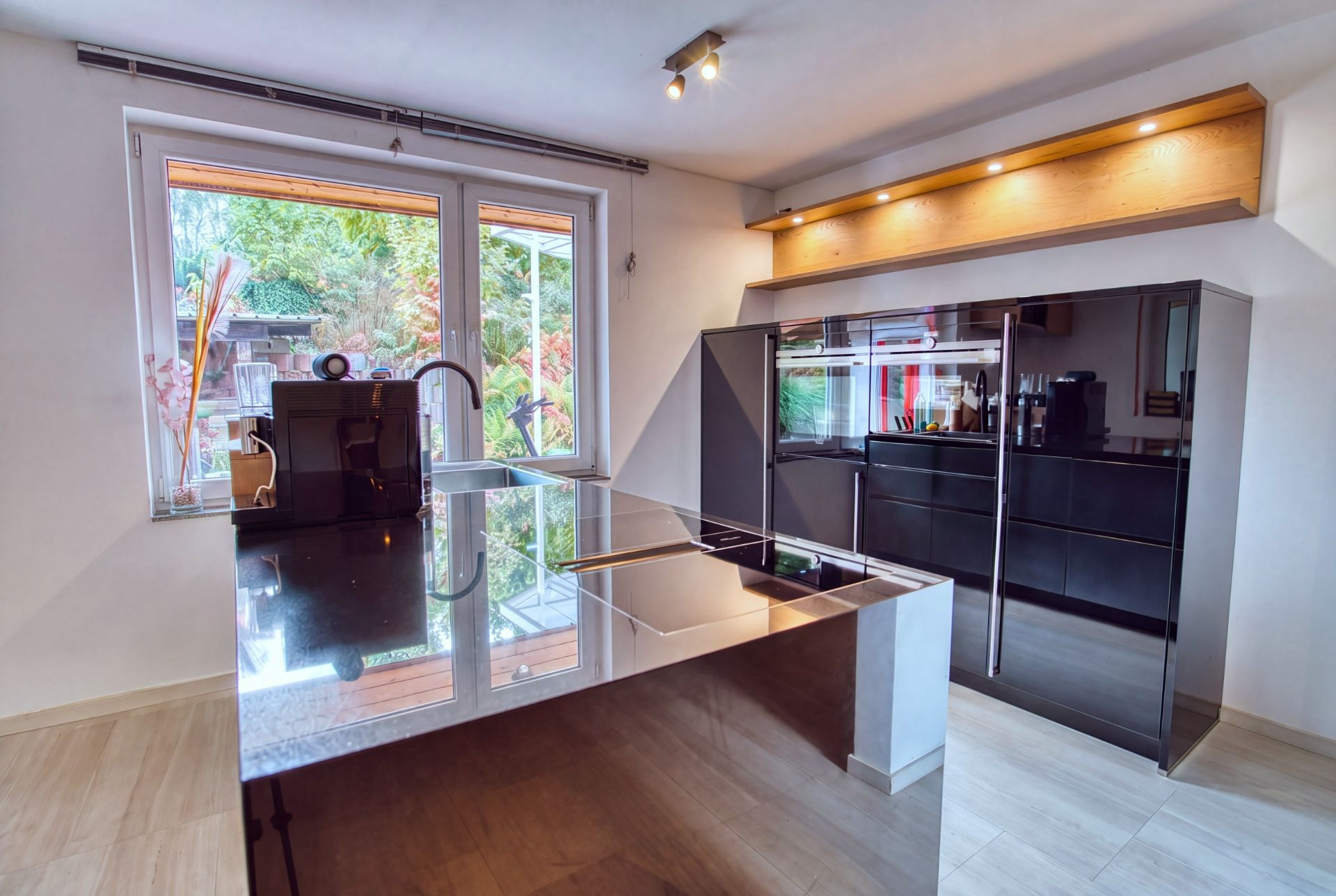 Moderne Küche mit glänzender Insel, großem Fenster und schwarzen Schränken.