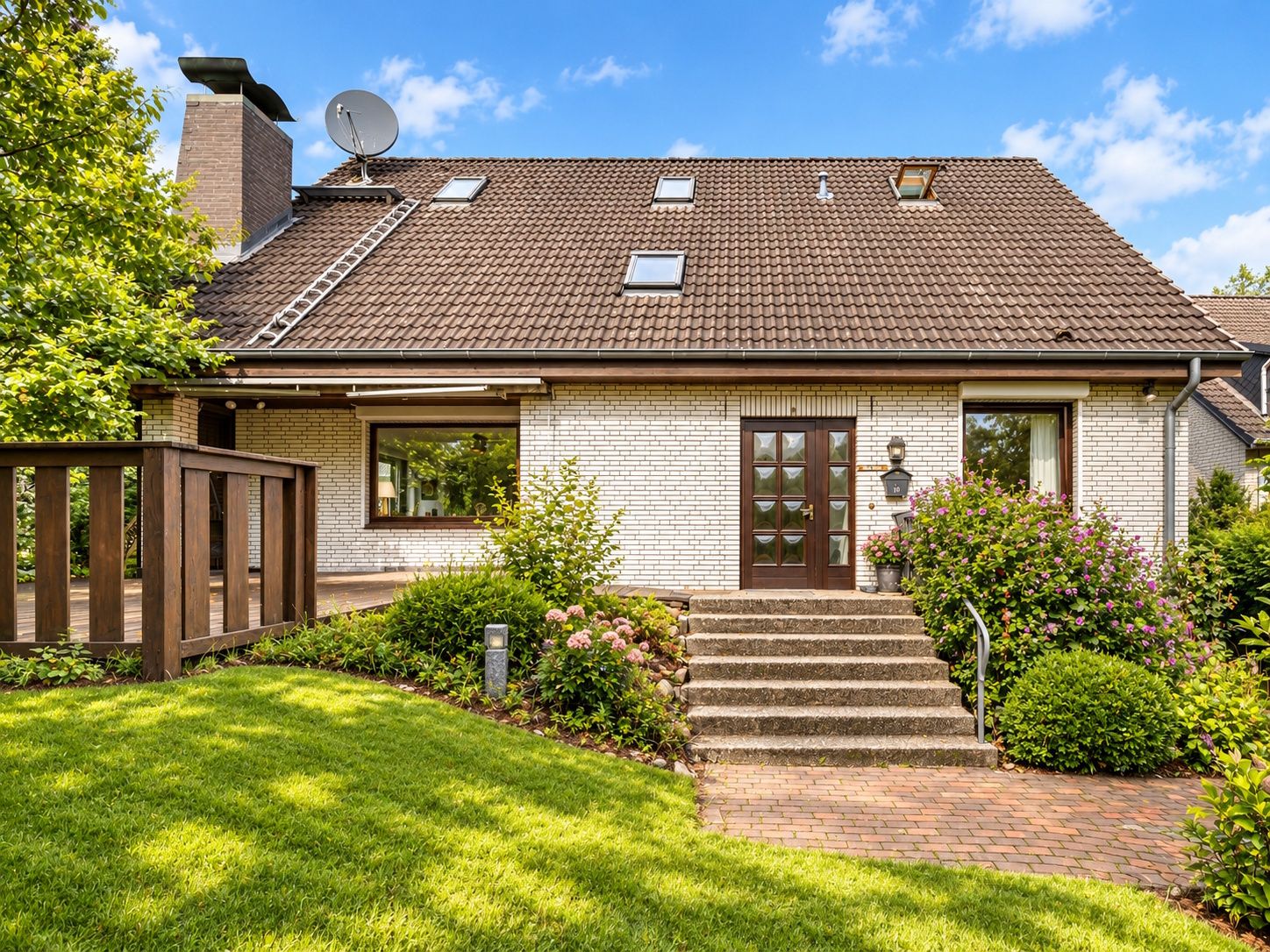Einfamilienhaus mit Treppe und Garten, Eingangstür in der Mitte, gepflegter Rasen und Sträucher.